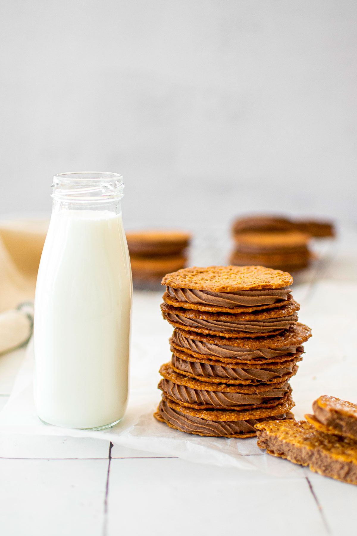 stack of chocolate peanut butter florentine sandwich cookies with a bottle of milk on a white tile counter.