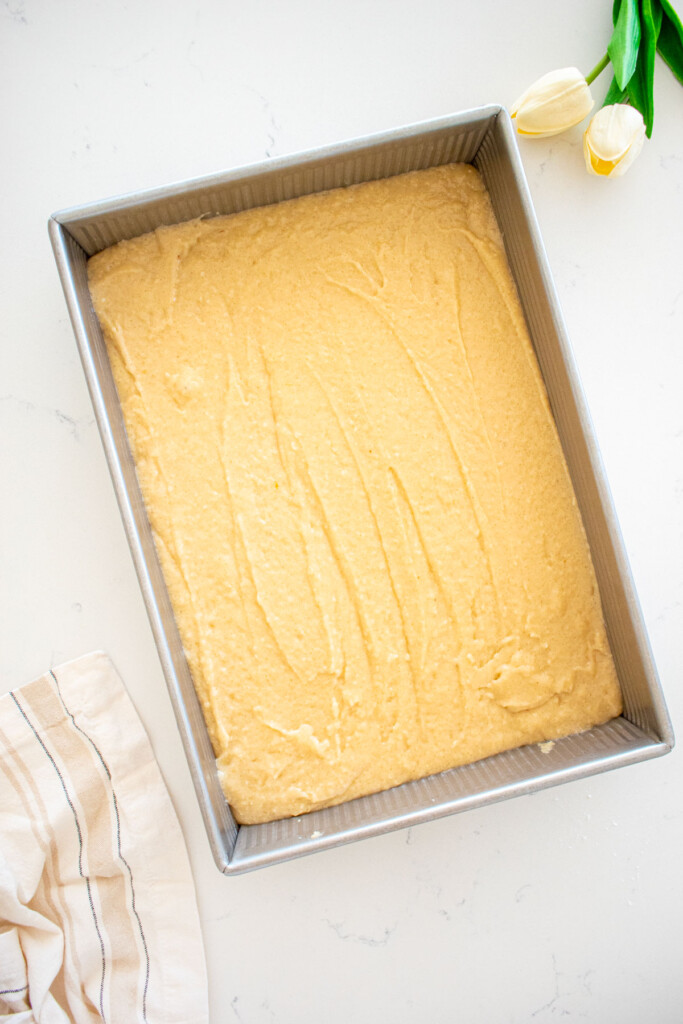 9x13-inch baking pan with eggless coconut cake batter spread evenly into it on a marble counter.