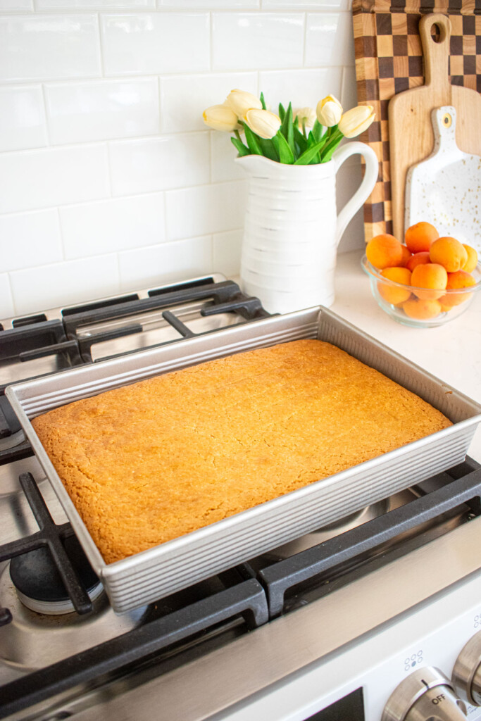 9x13 in baking pan with baked eggless coconut sheet cake cooling on top of an oven.