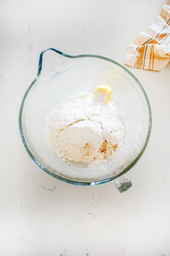 ingredients for coconut buttercream frosting in a glass mixing bowl on a marble counter.