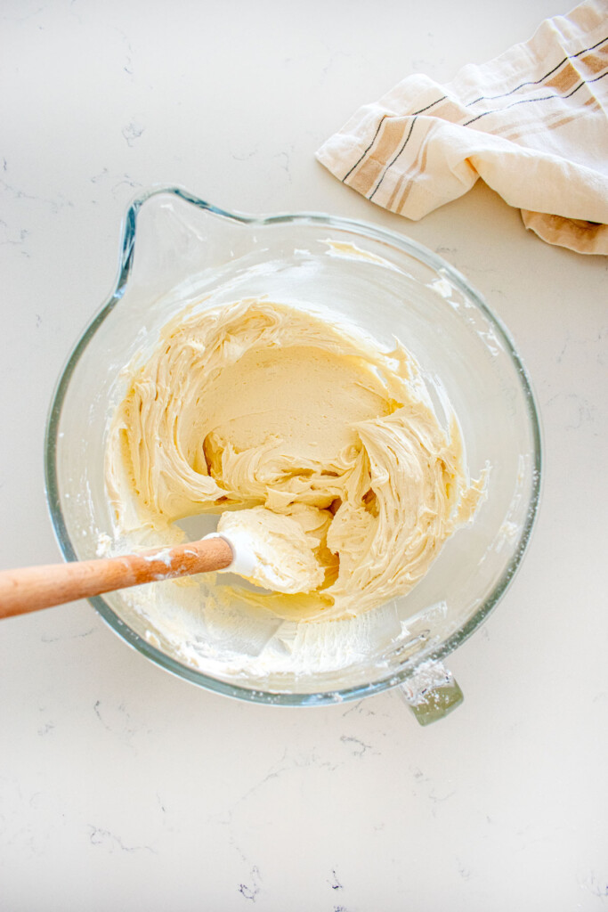 smooth and creamy coconut buttercream in a glass mixing bowl with a spatula on a marble counter.