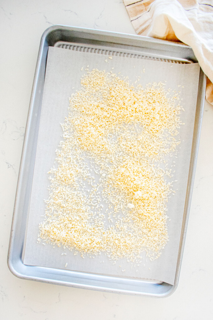baking sheet with parchment paper and fine shredded coconut on top on a marble counter.