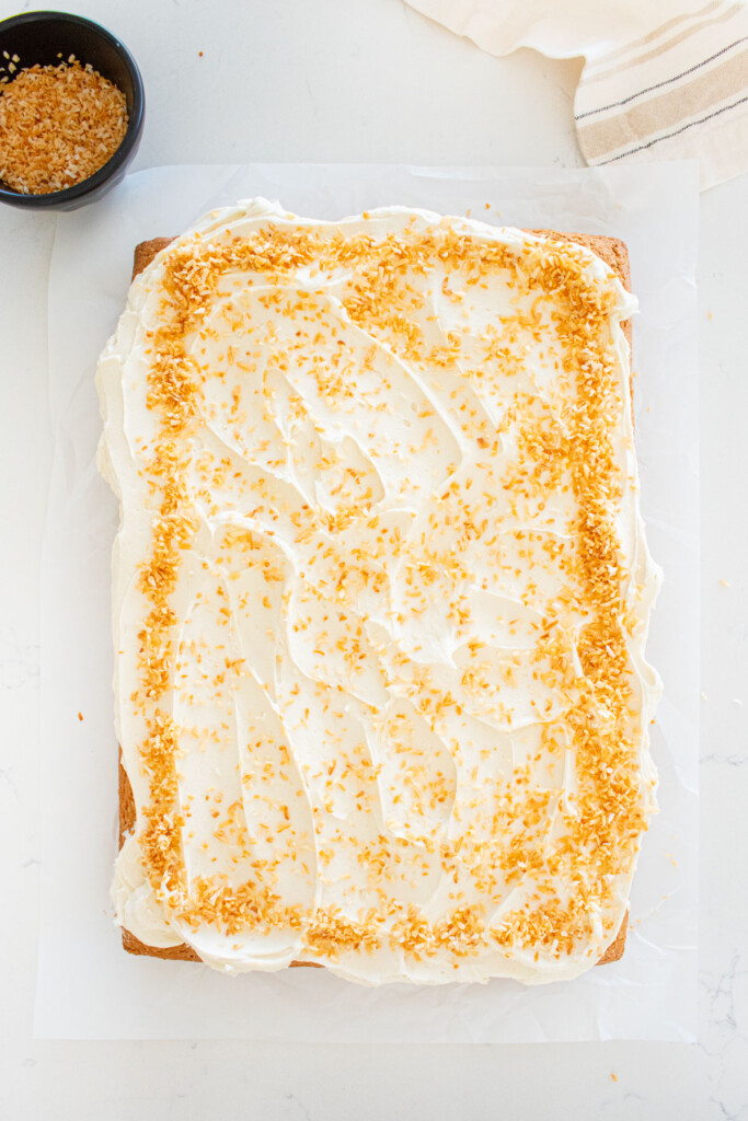 eggless coconut sheet cake with coconut buttercream and toasted coconut on a marble counter.