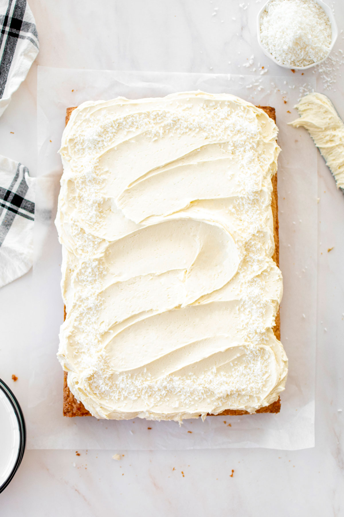 eggless coconut sheet cake with coconut buttercream on a marble counter.