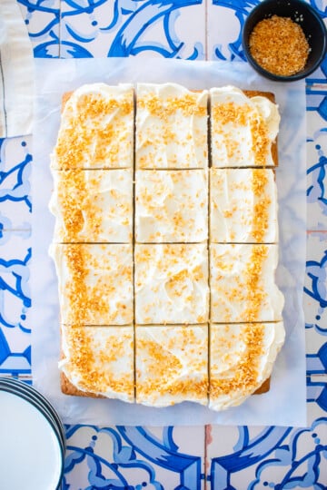 eggless coconut sheet cake sliced into square slices on a blue tile table.
