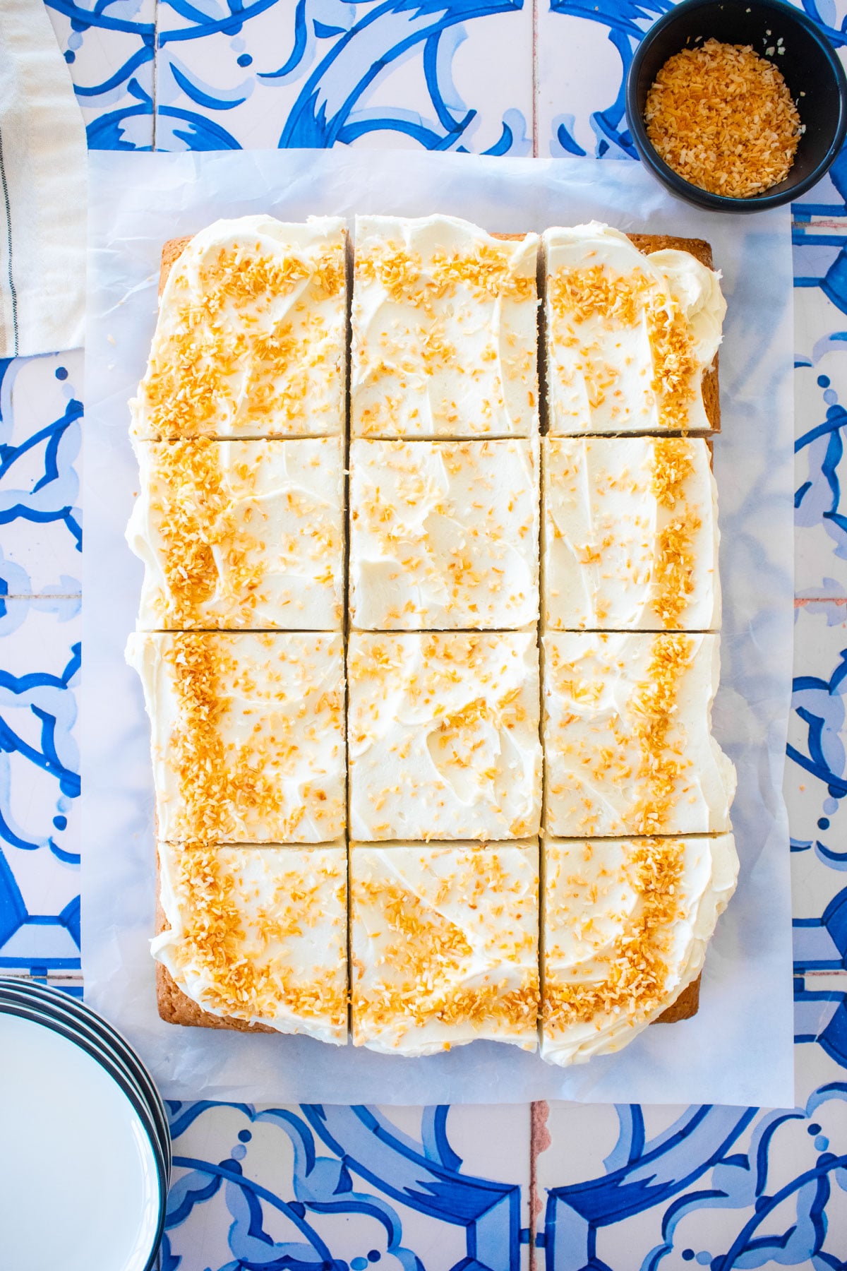eggless coconut sheet cake sliced into square slices on a blue tile table.