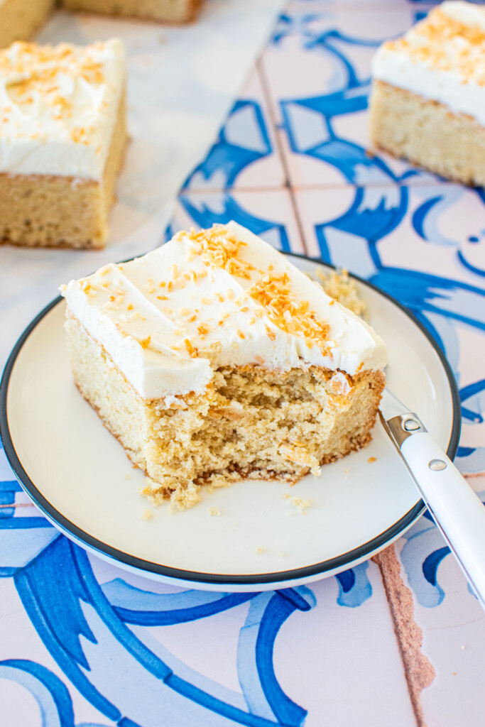 square slice of eggless coconut sheet cake with coconut buttercream and toasted coconut on a plate with a fork.