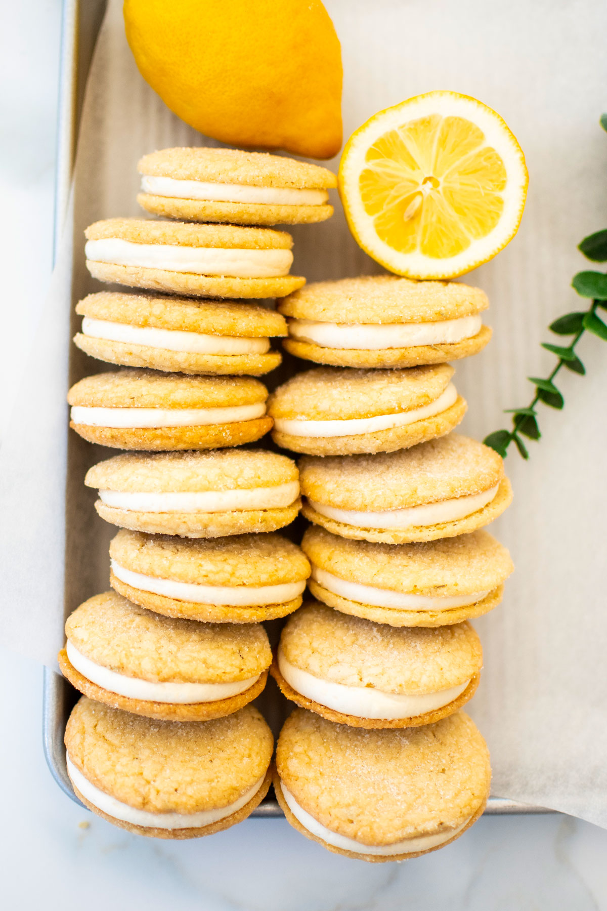lemon rosemary sandwich cookies on a baking sheet with fresh lemon on a marble counter.