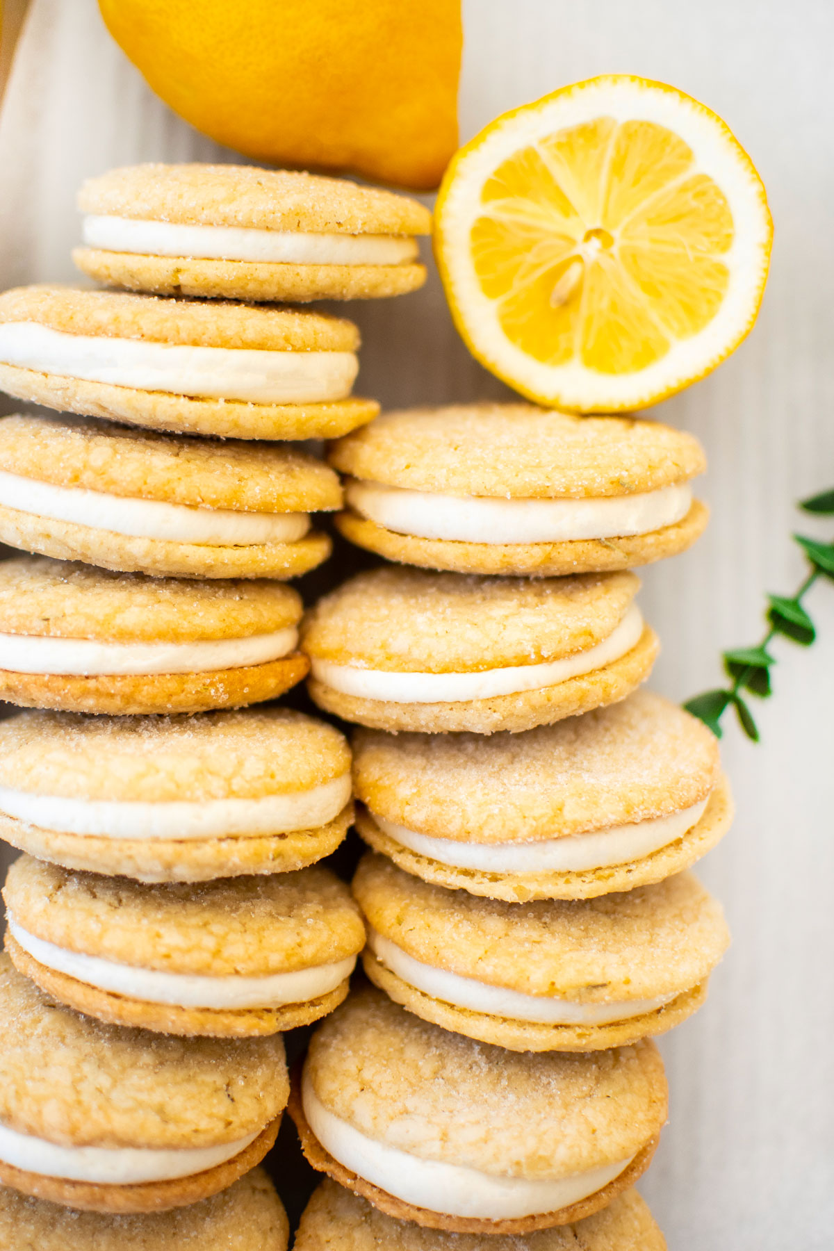 lemon rosemary sandwich cookies on a baking sheet with fresh lemon on a marble counter.