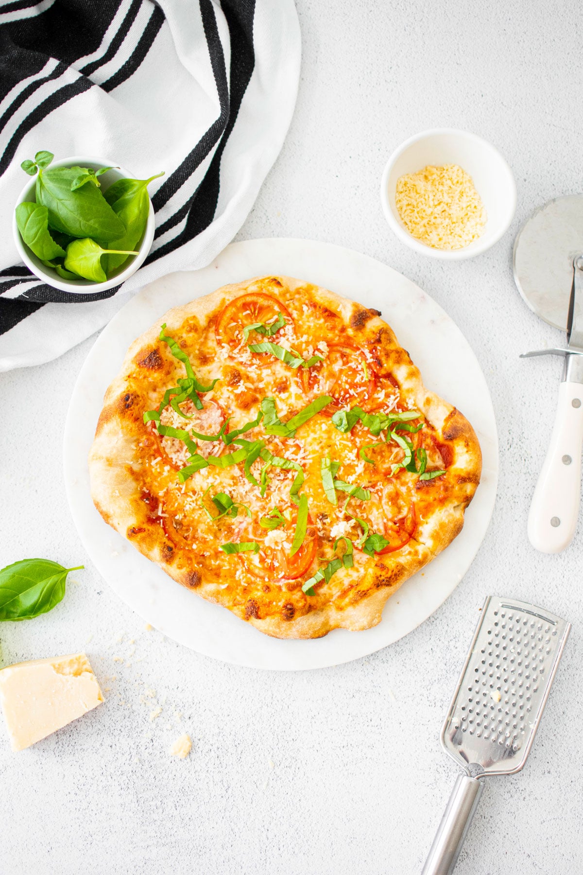 margarita pizza on a white marble serving board with fresh basil and parmesan on a white marble counter.