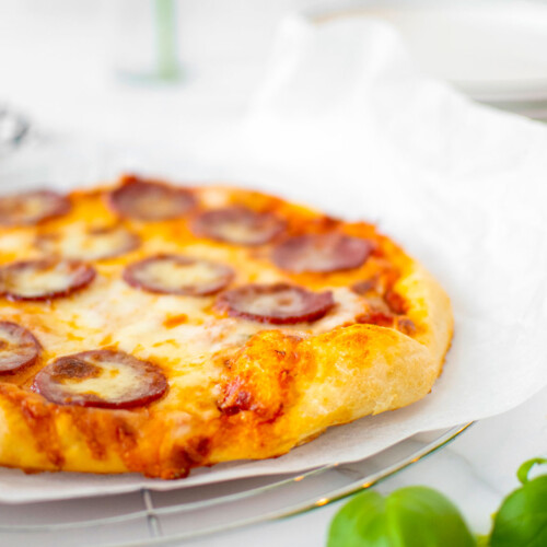 pepperoni pizza on a cooling rack on a white marble counter.