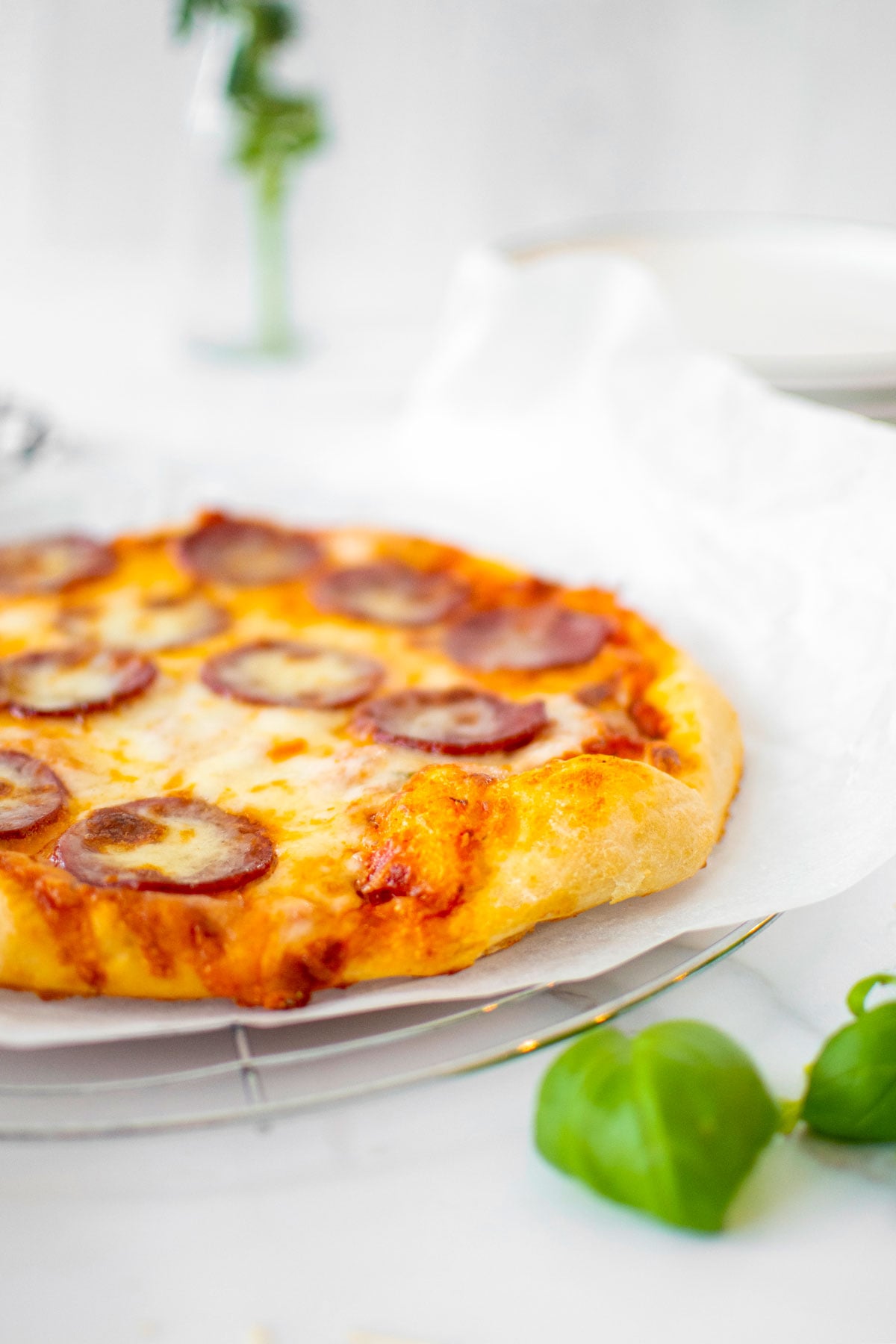 pepperoni pizza on a cooling rack on a white marble counter.