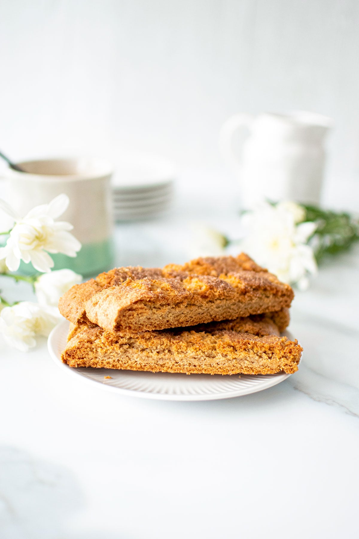 snickerdoodle biscotti on a white marble counter with a mug of coffee and fresh flowers.