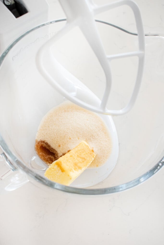 butter sugar and vanilla in a glass mixing bowl on a white marble counter.