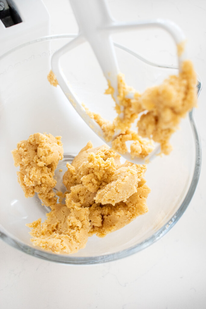 snickerdoodle biscotti cookie dough in a glass mixing bowl on a white marble counter.