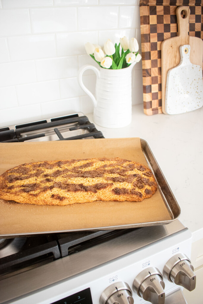 snickerdoodle biscotti log baked, cooling on a baking sheet on top of an oven.