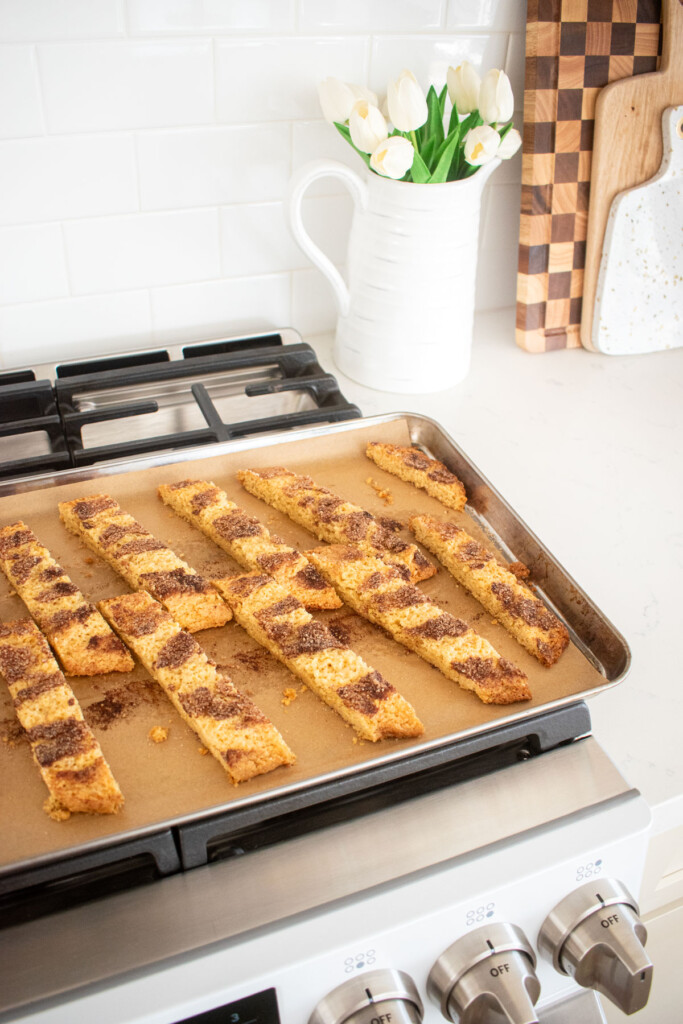 baked snickerdoodle biscotti cooling on a baking sheet on top of an oven.