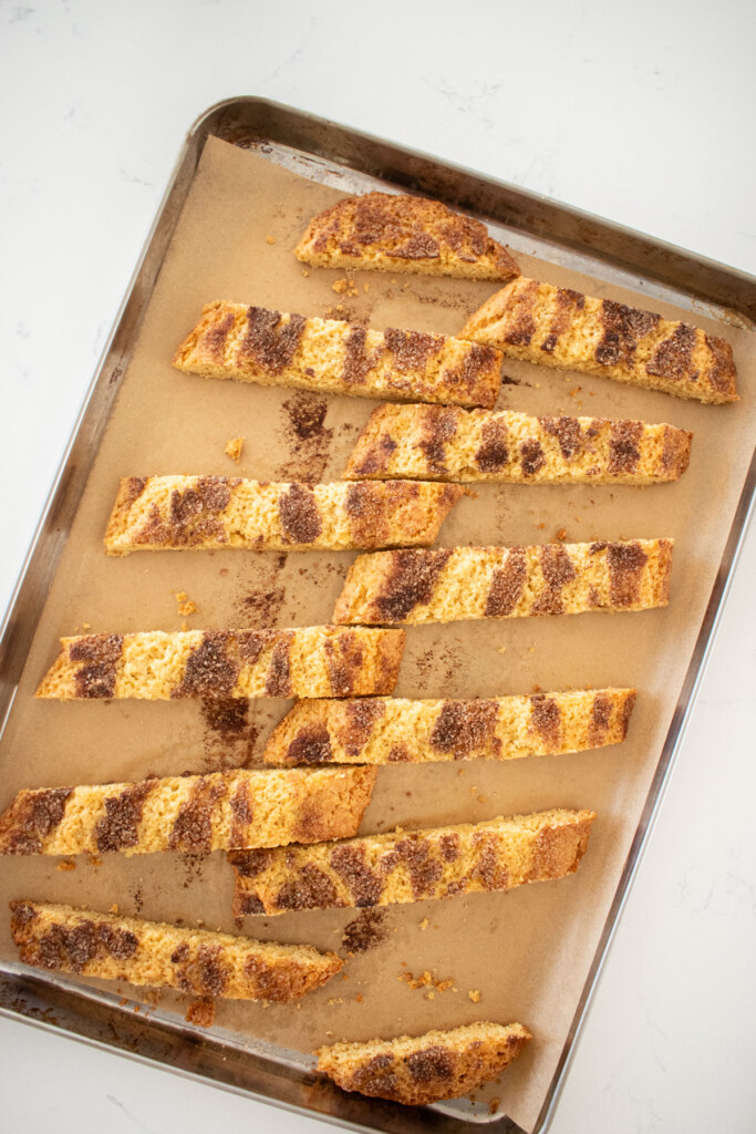 snickerdoodle biscotti cut into pieces on a baking sheet on a white marble counter.