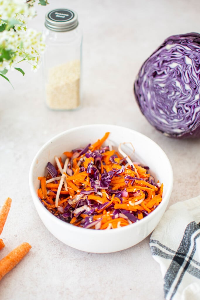 cabbage, carrot and bean sprouts slaw in a white bowl on a light pink background.
