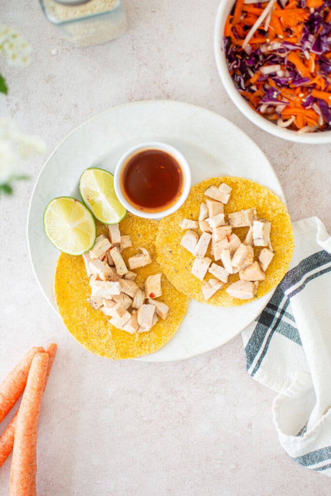 plate with corn tortillas, chicken and limes with a bowl of sweet chili slaw.