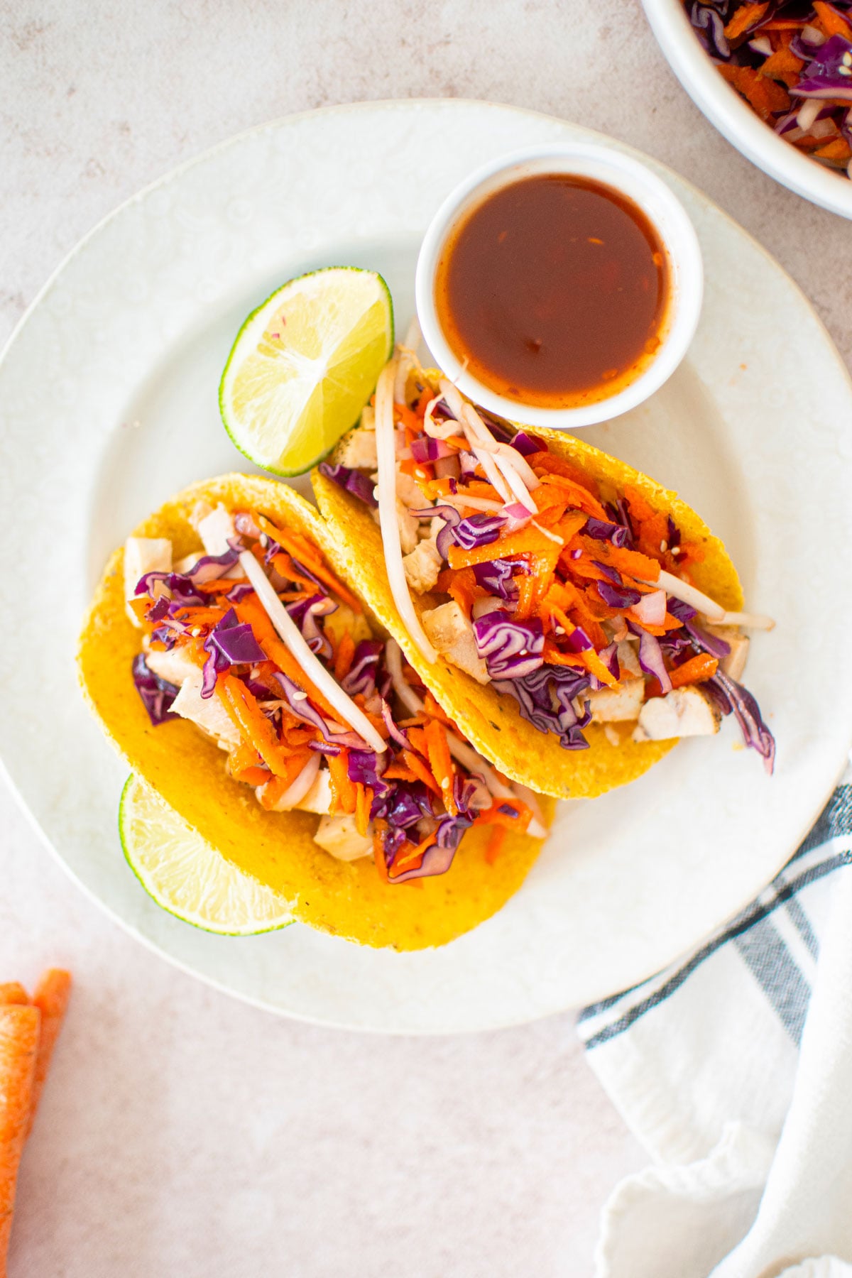 sweet chili chicken soft tacos on a white plate with a dipping bowl of sweet chili and limes.