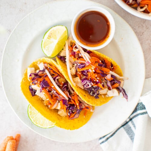 sweet chili chicken soft tacos on a white plate with a dipping bowl of sweet chili and limes.