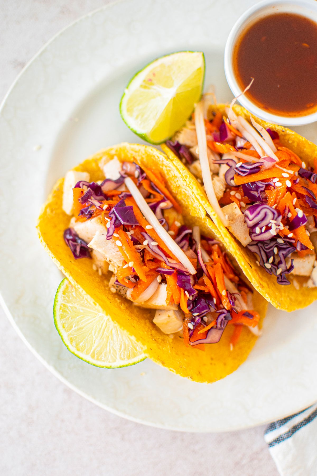 sweet chili chicken soft tacos on a white plate with a dipping bowl of sweet chili and limes.