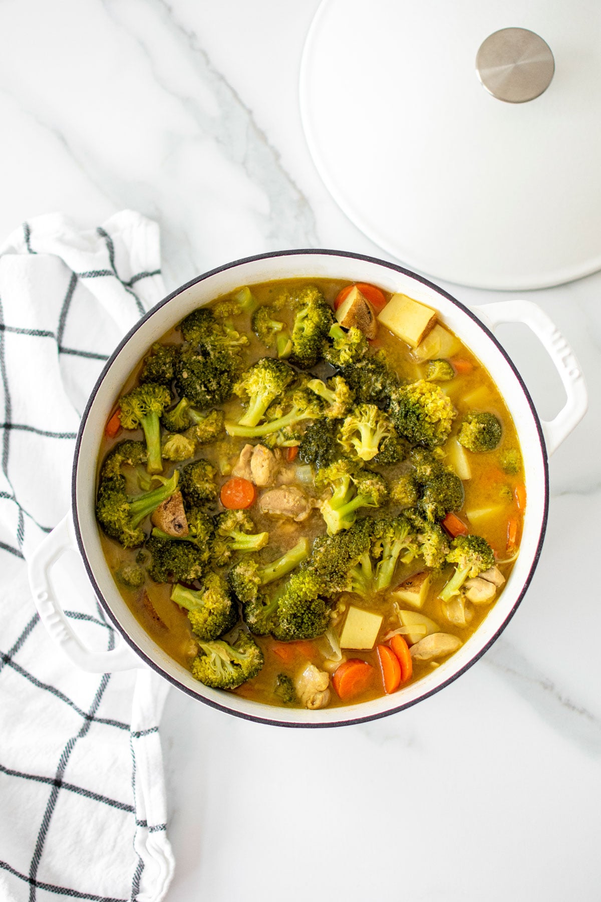 yellow curry chicken with bone broth in a white dutch oven on a marble countertop.