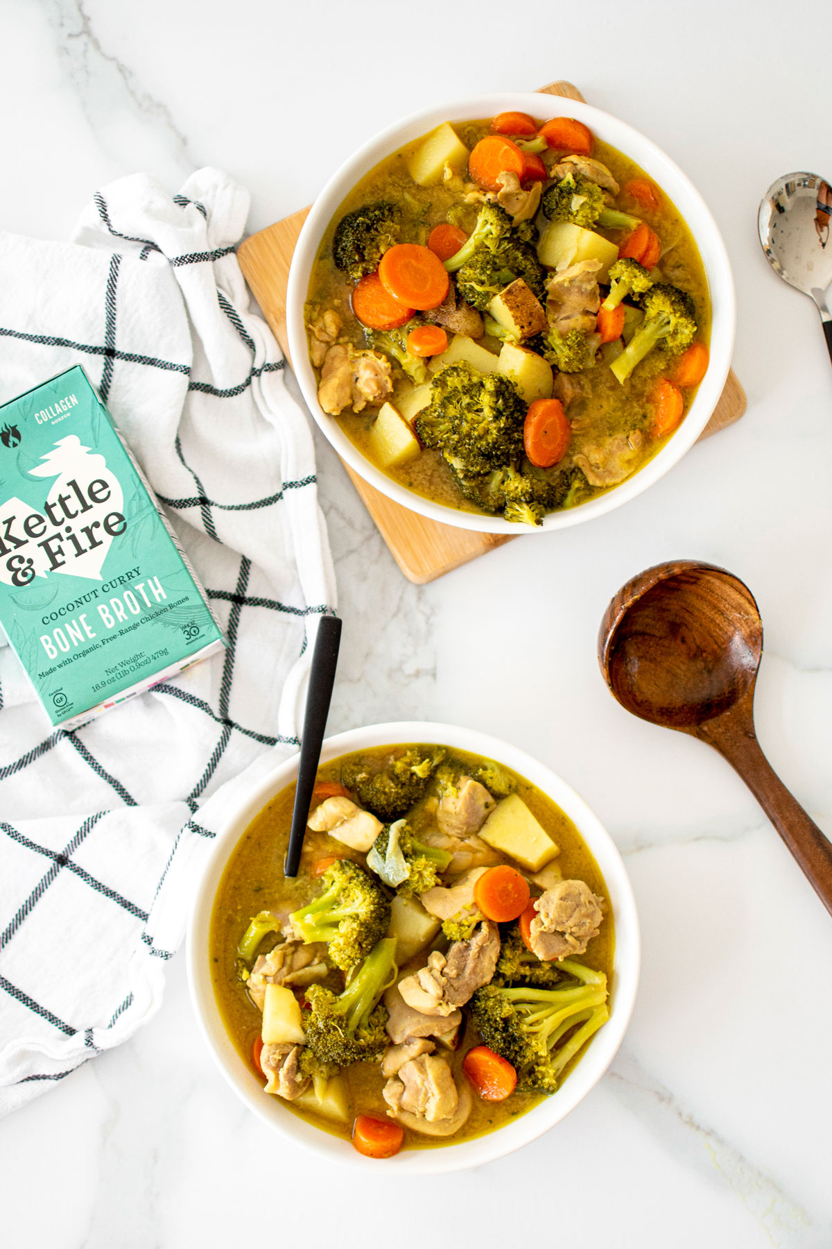 two bowls of yellow curry chicken on a white marble countertop.