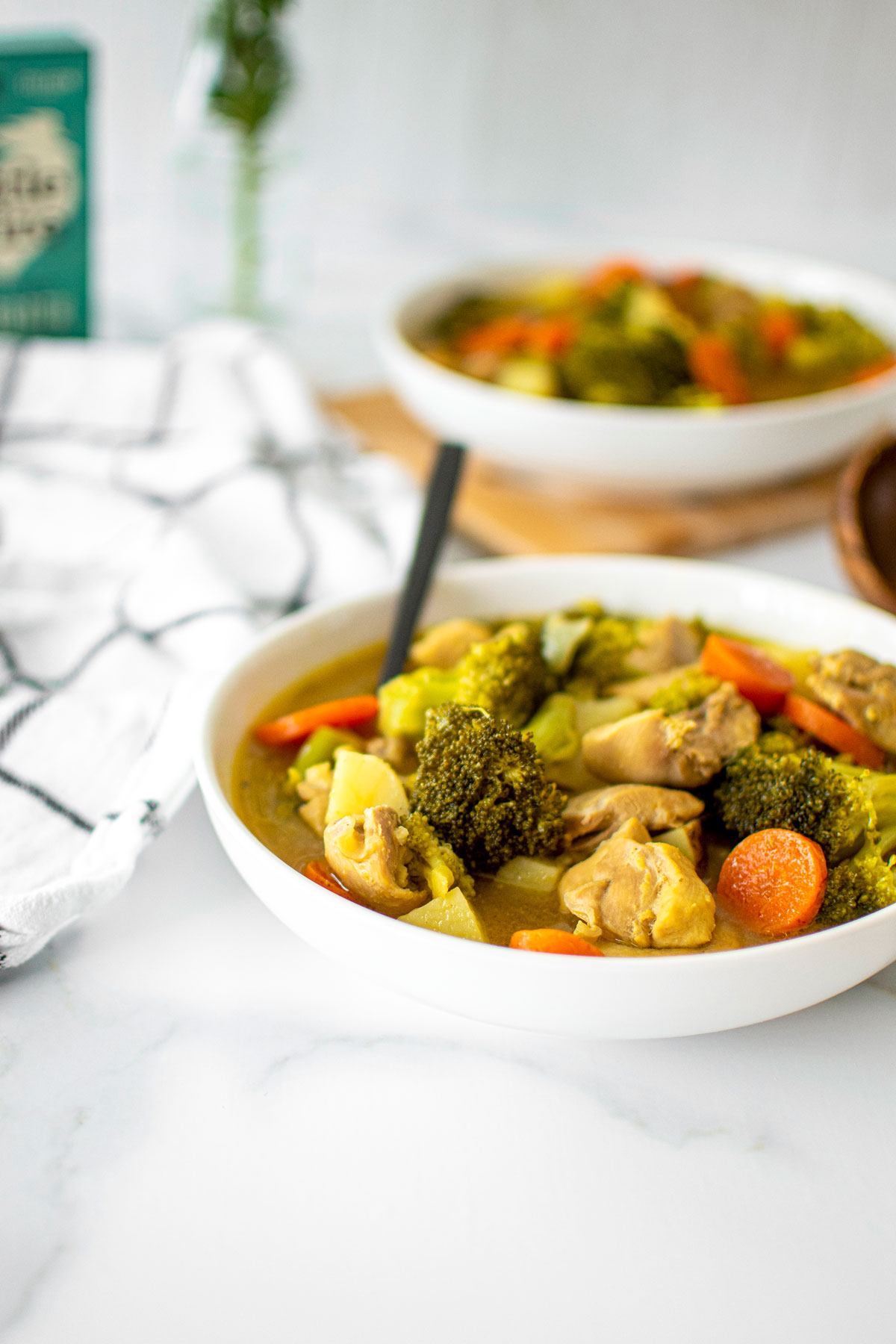 two bowls of yellow curry chicken on a white marble countertop.