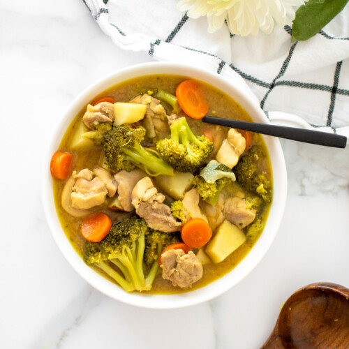 bowl of yellow curry chicken with a spoon on a white marble countertop.