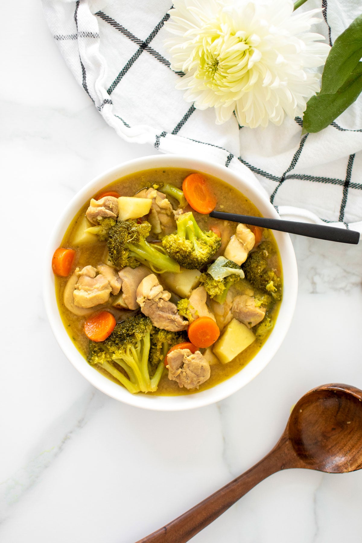 bowl of yellow curry chicken with a spoon on a white marble countertop.