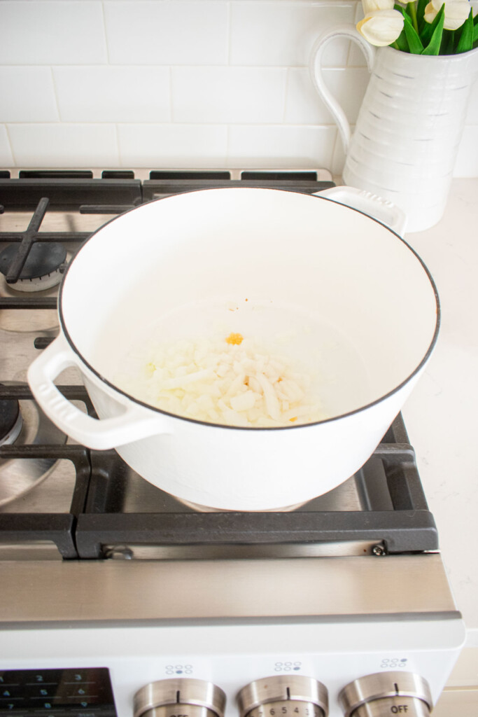 garlic and onions in a white dutch oven on a stovetop.