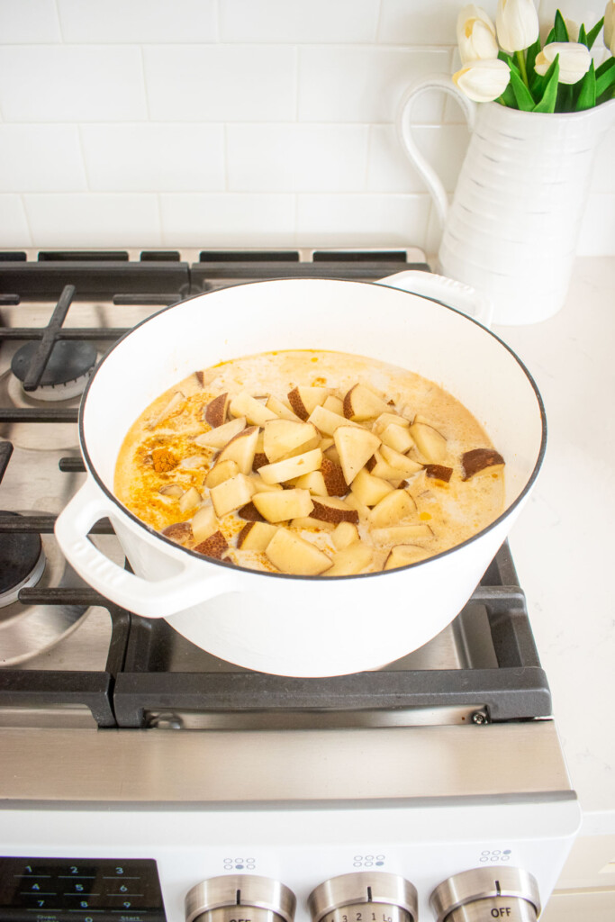 yellow curry chicken with bone broth cooking in a dutch oven on a stovetop.