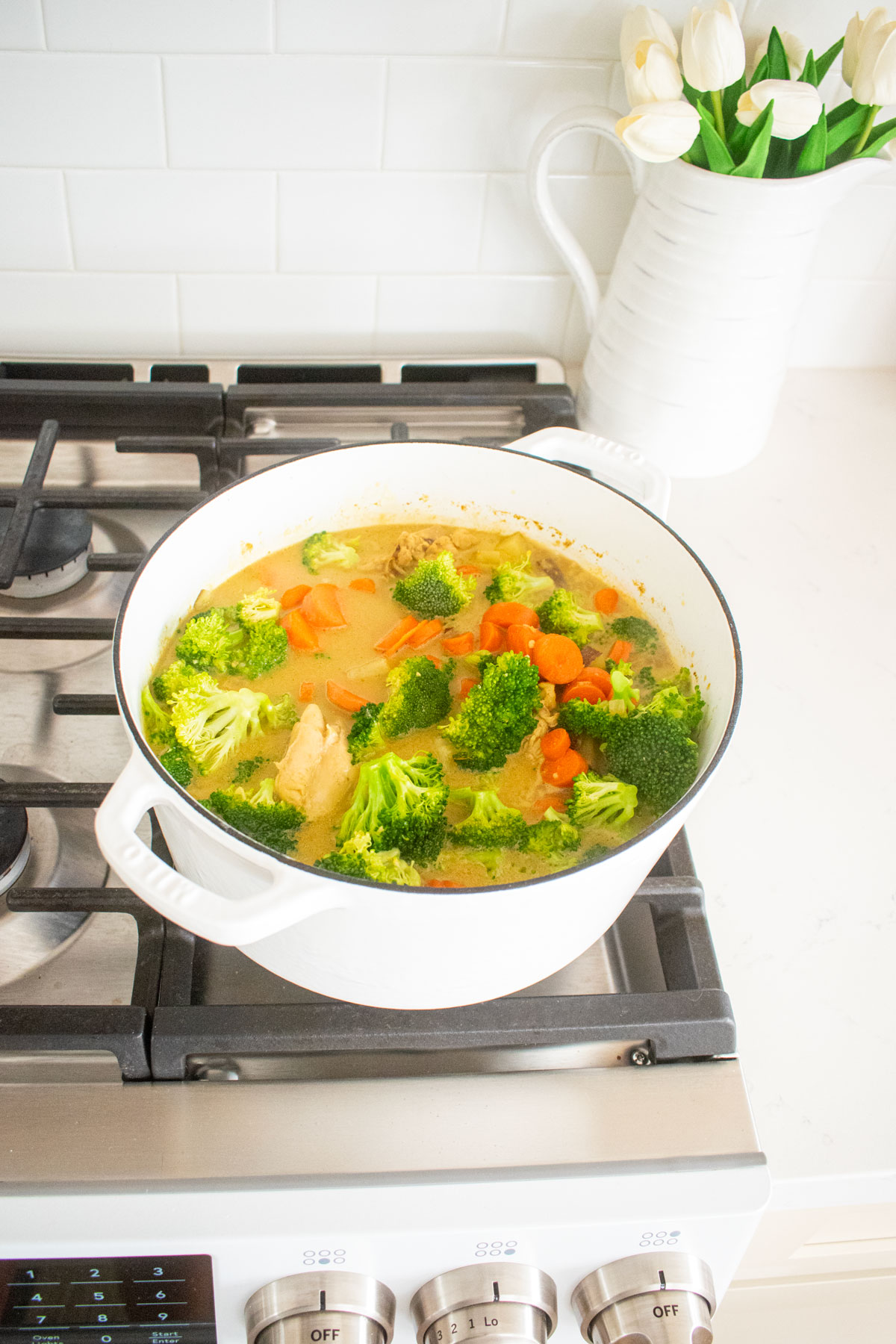 yellow curry chicken simmering in a white dutch oven on a stovetop.