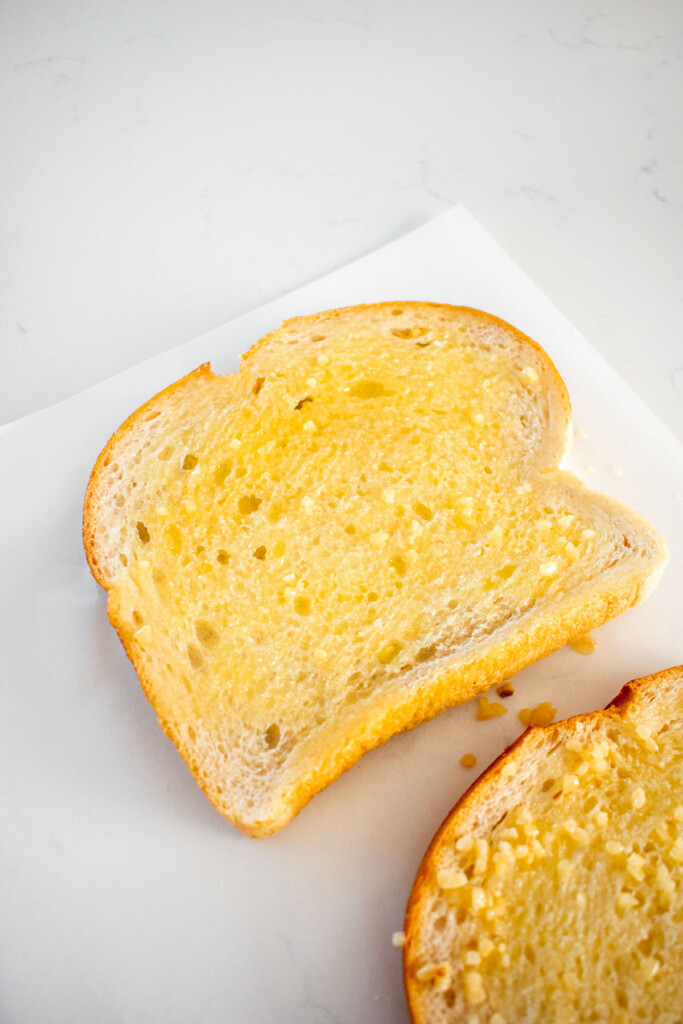 sourdough bread slices with melted butter and garlic on parchment paper on a marble counter.