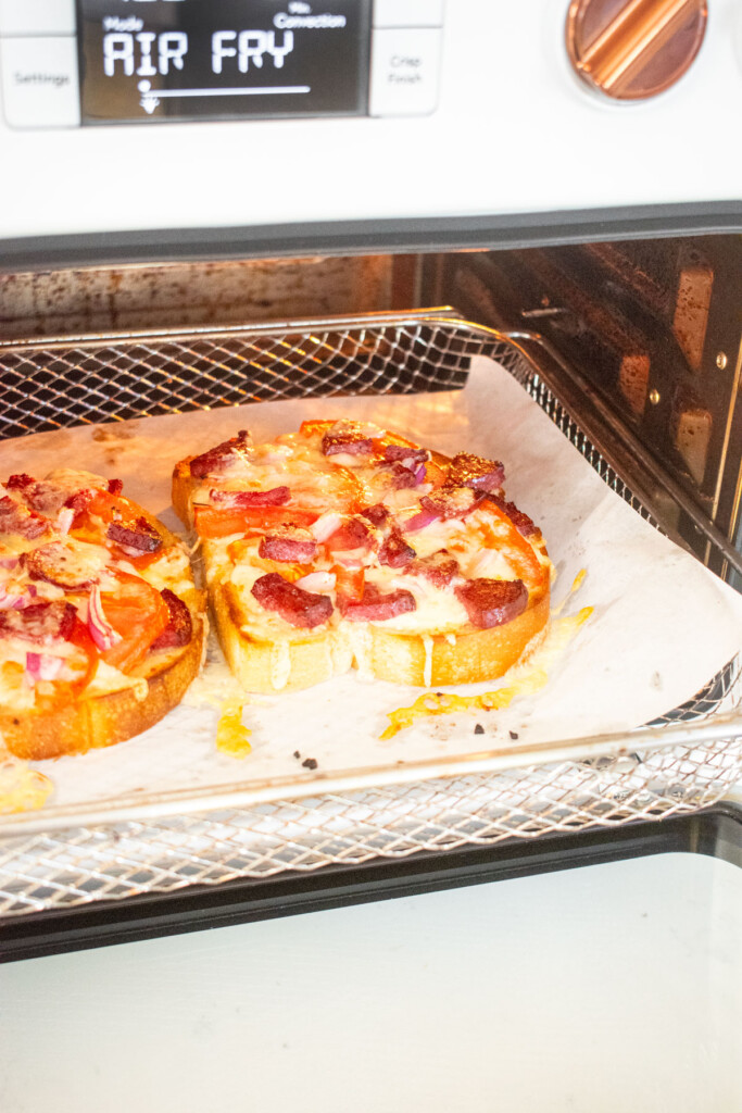 loaded garlic bread slices in an air fryer with melty golden brown cheese.