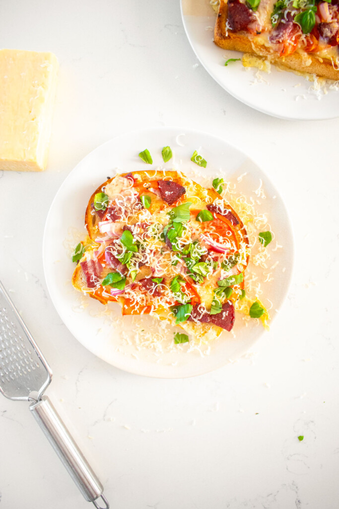 air fryer loaded garlic bread on a plate with fresh basil and parmesan on a marble counter.