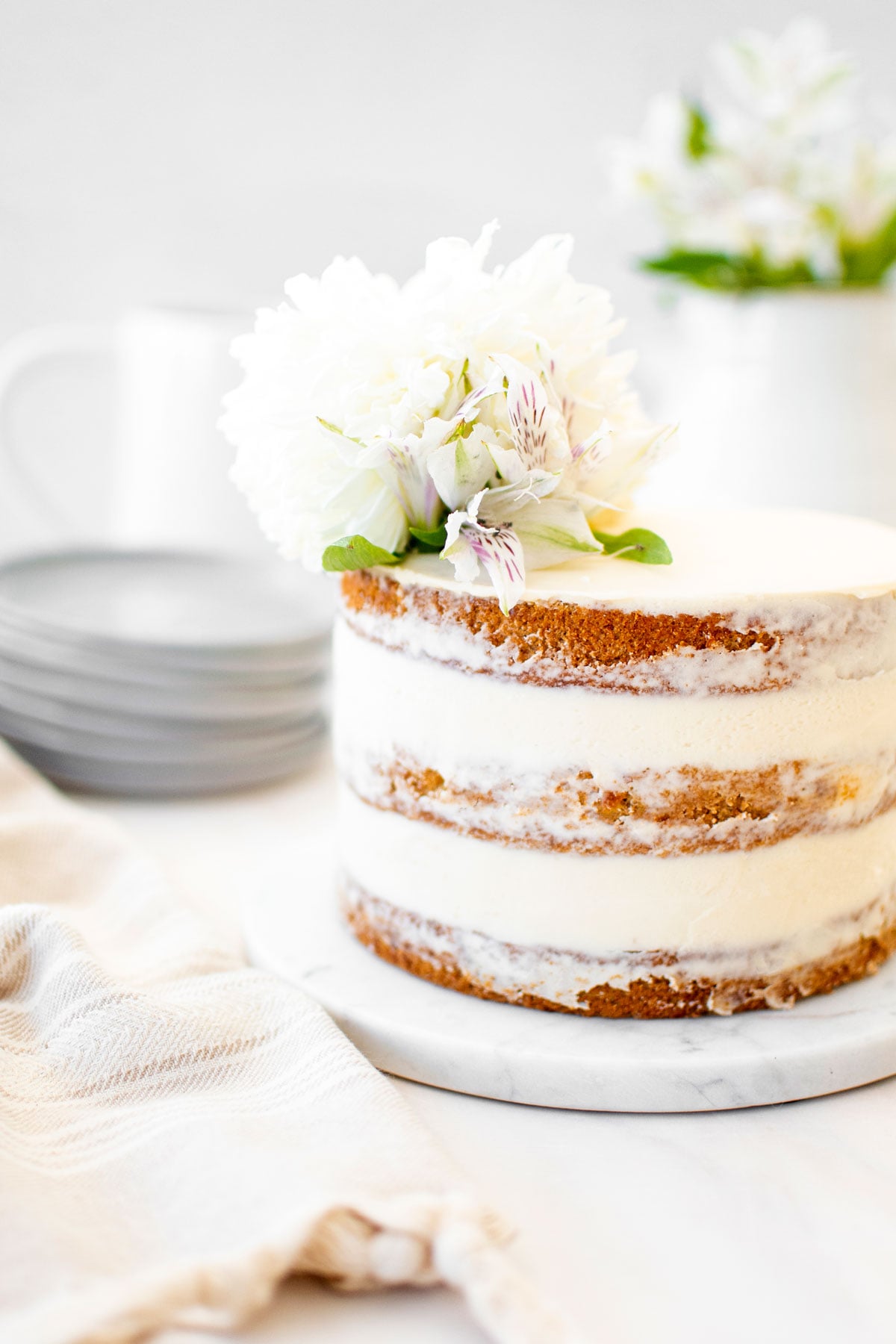 banana bread semi naked cake on a marble cake plate with fresh flowers on top.
