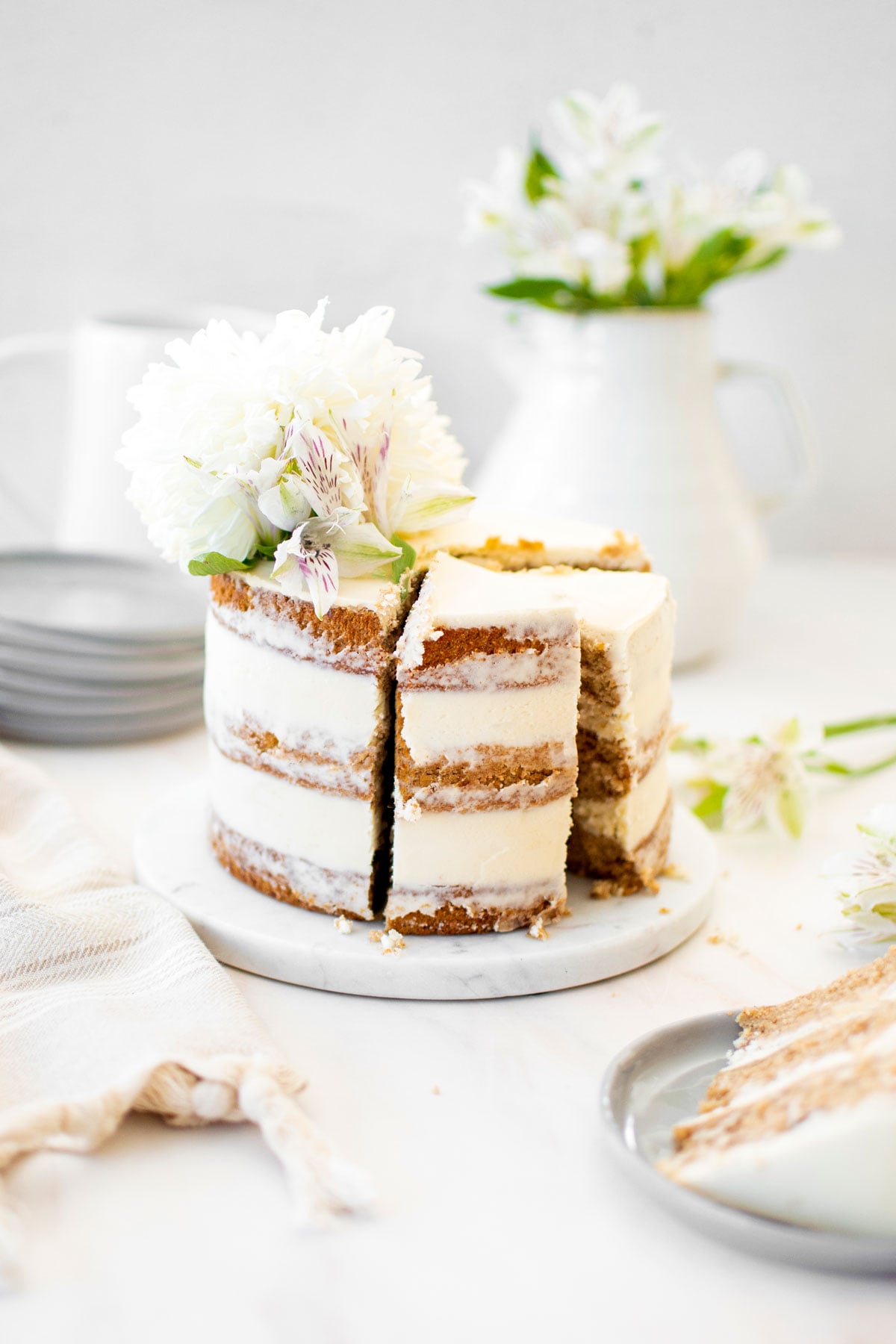banana bread semi naked cake on a cake plate cut into slices with fresh flowers on top.