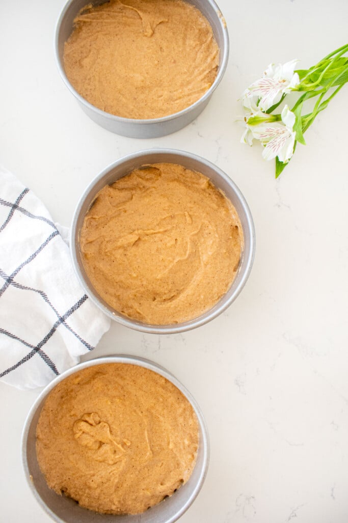 three 6-inch cake pans with banana bread cake batter in them on a white marble counter.