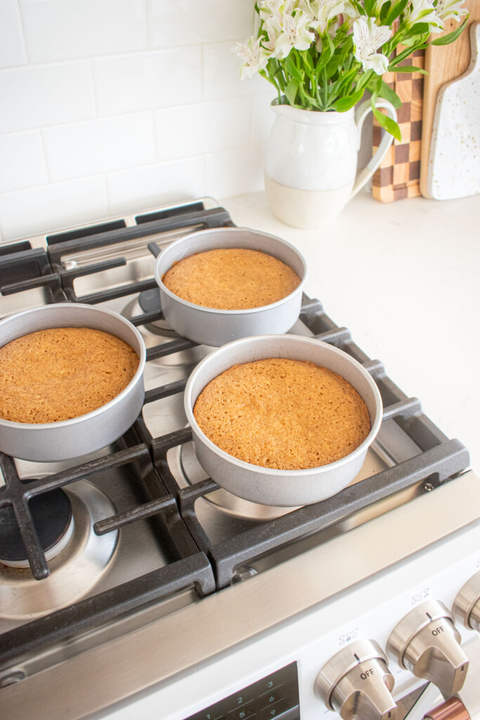 baked banana bread cakes in three 6-inch cake pans cooling on top of an oven.