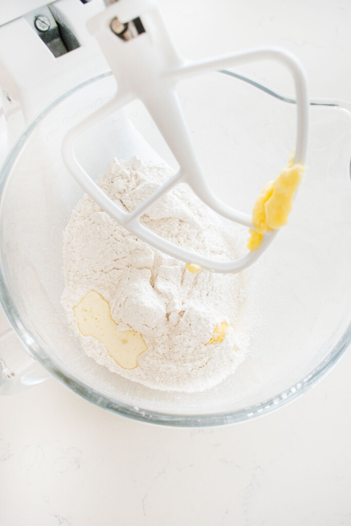 ingredients for buttercream frosting in a glass stand mixing bowl on a white marble counter.