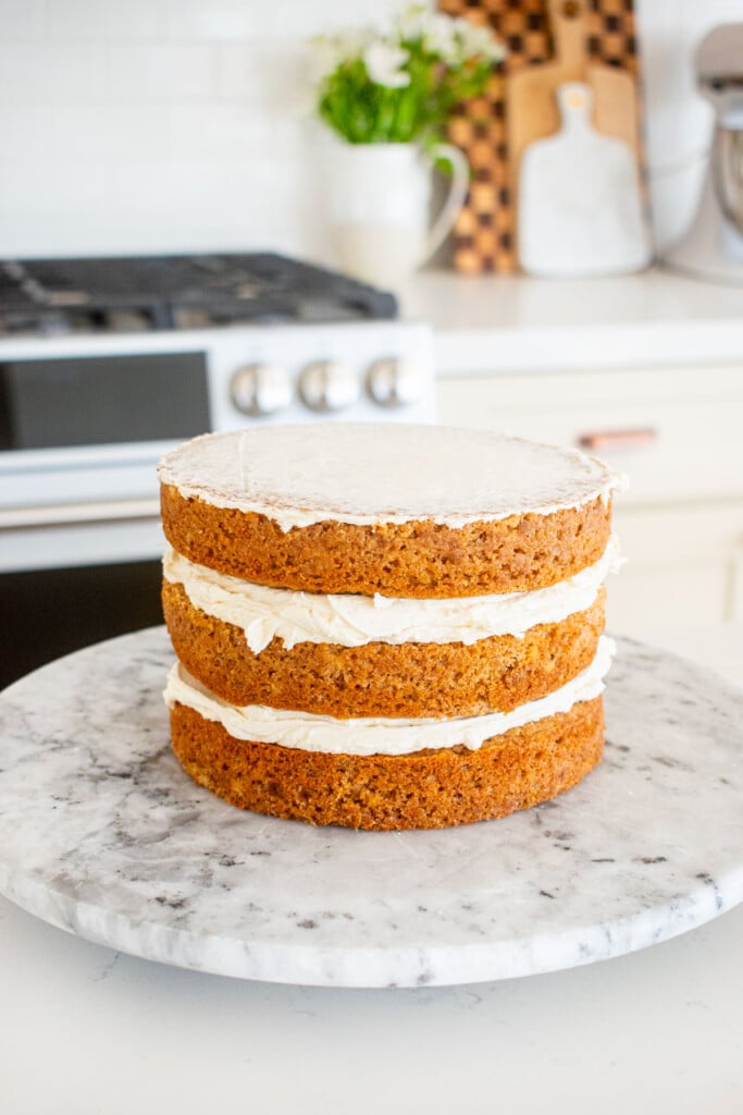 banana bread semi naked cake being assembled on a marble cake spinner on a white marble counter.