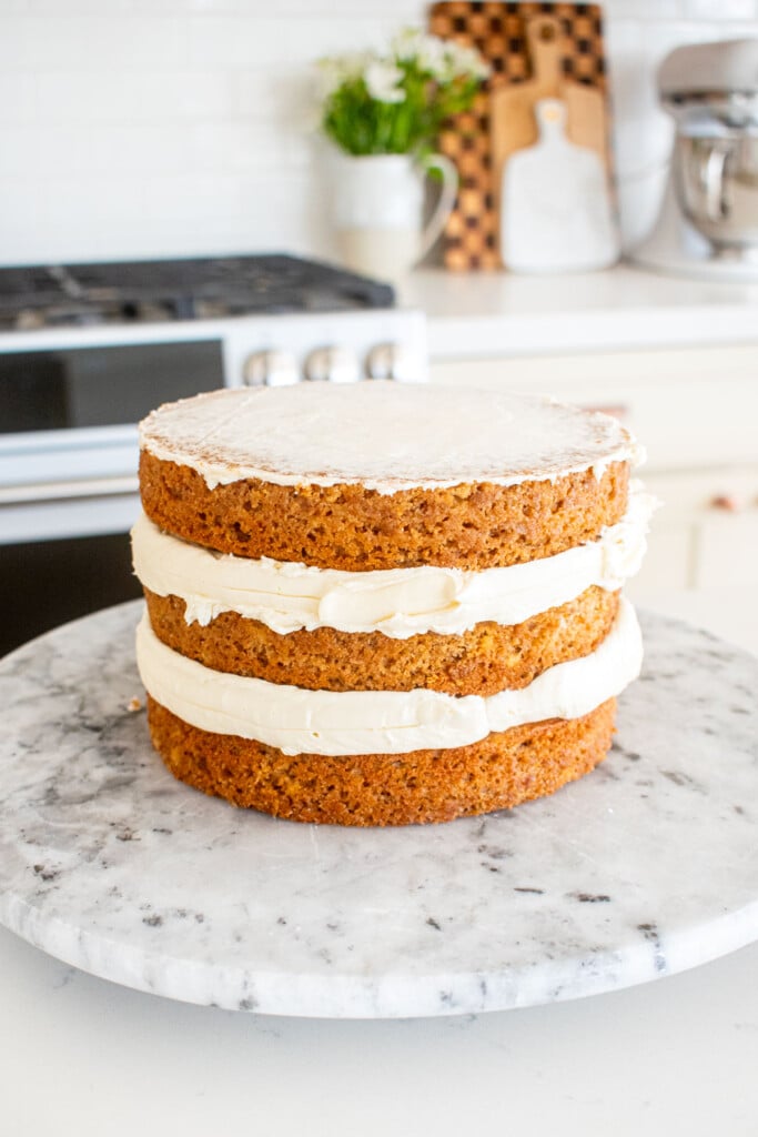 banana bread semi naked cake being assembled on a marble cake spinner on a white marble counter.