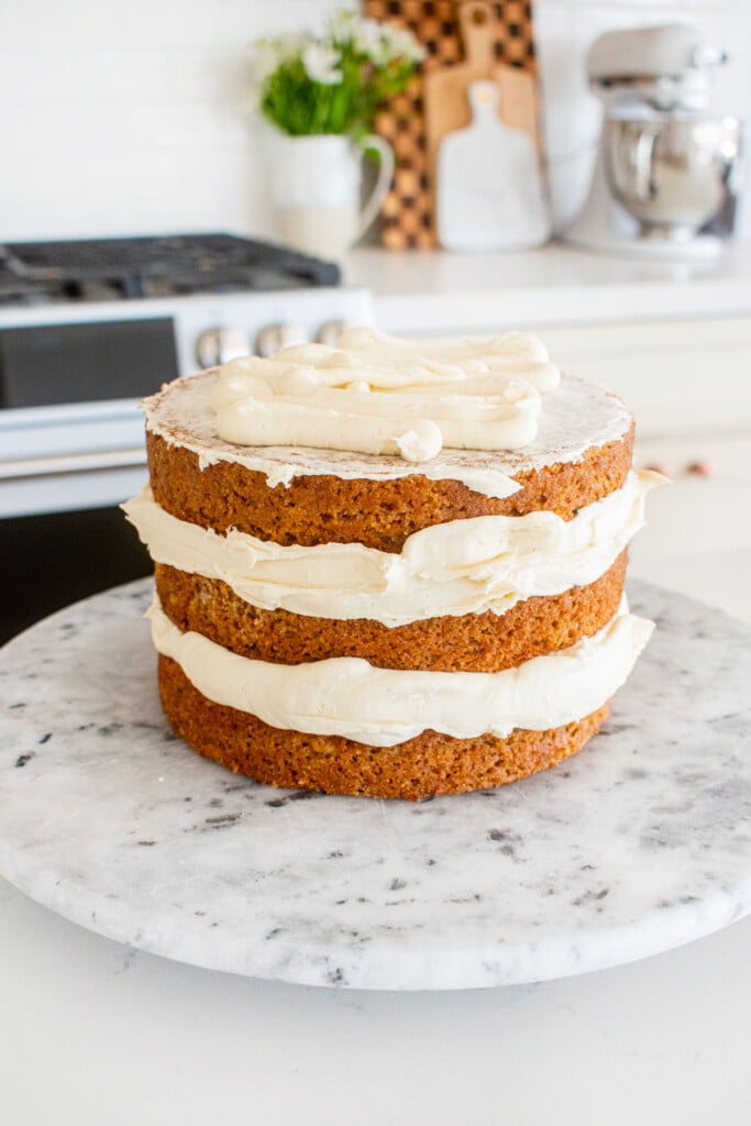 banana bread semi naked cake being assembled on a marble cake spinner on a white marble counter.