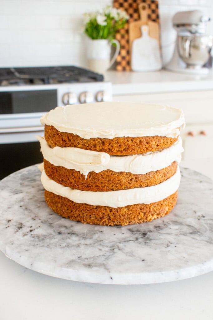 banana bread semi naked cake being assembled on a marble cake spinner on a white marble counter.