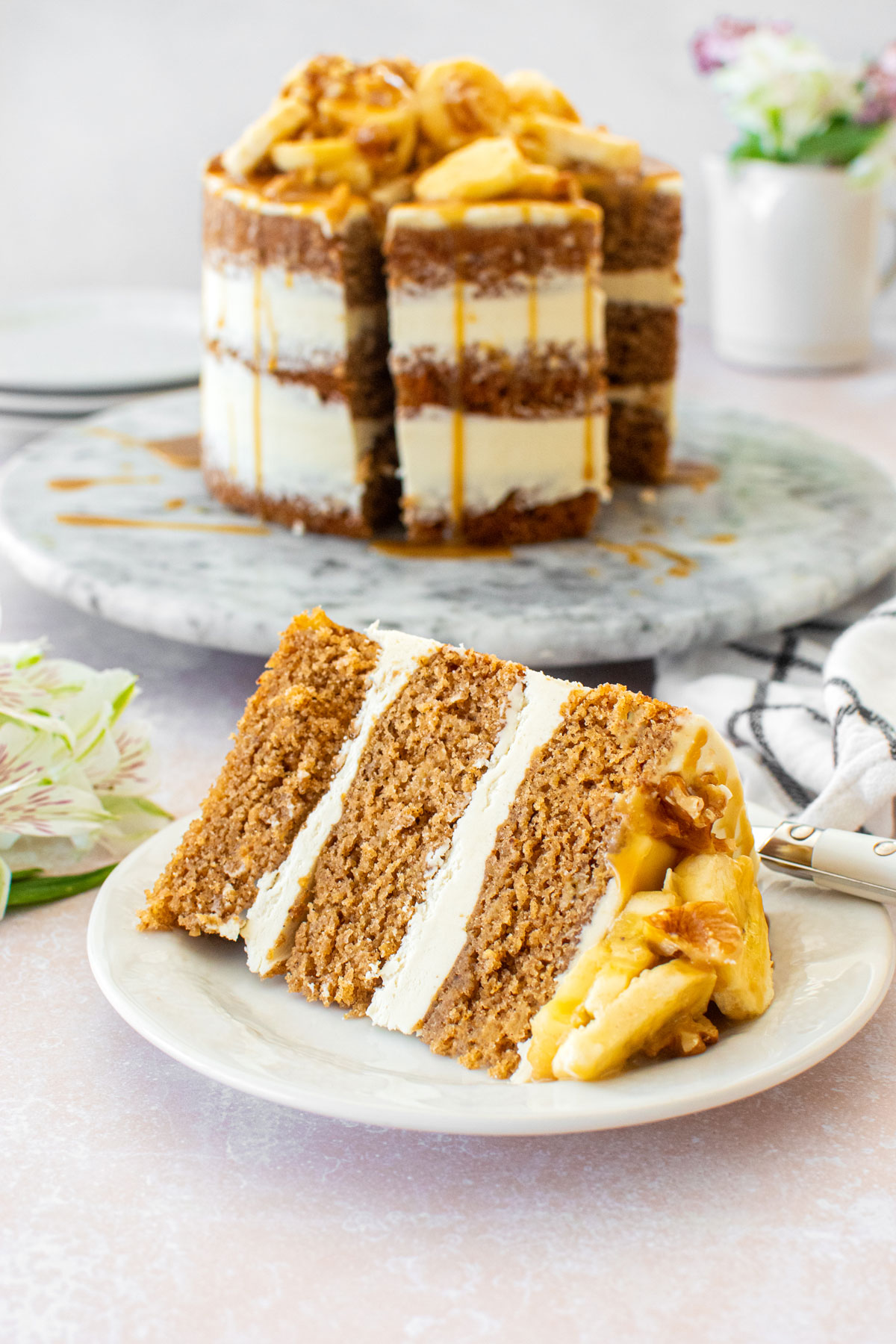 slice of banana bread semi naked cake on a plate on a table with fresh flowers.