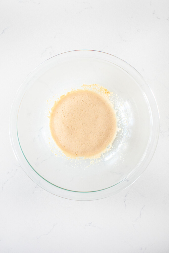 yeast and water in a glass mixing bowl on a white marble counter.