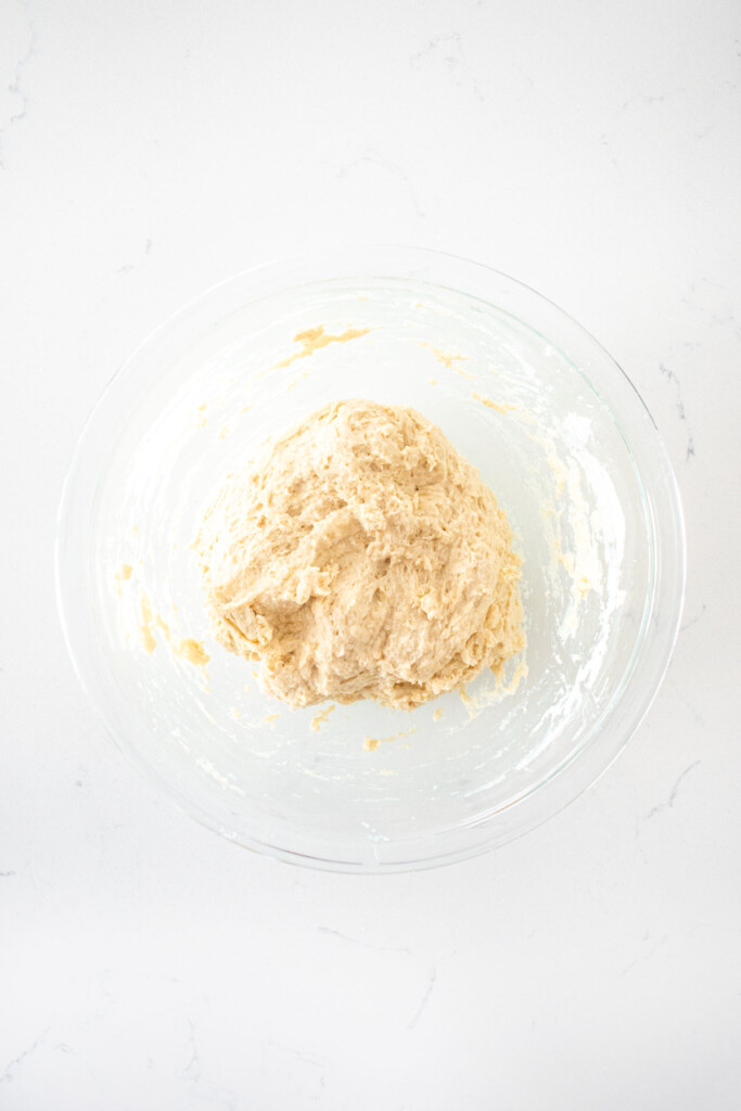 chicago style thin crust pizza dough in a glass mixing bowl on a white marble counter.